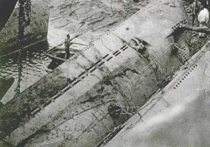 A la izquierda, al centro, se ve la proa del U61. En el centro aparece el U554 con varias cargas magn&eacute;ticas de demolici&oacute;n adosadas al casco. 